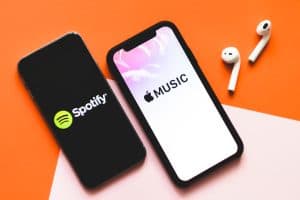手拿著 iPhone X 與 Apple 音樂應用程序和 Spotify 的屏幕截圖。Apple Music 和 Spotify 是最受歡迎的音樂流媒體服務。
